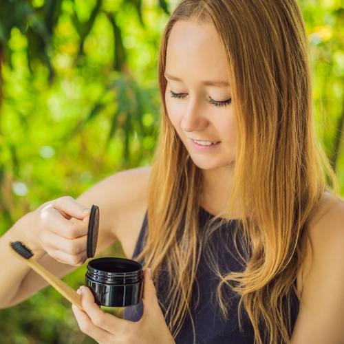 Kvinna med tandborste och Diamond Smile tandblekningspulver med aktivt kol Coco Powder